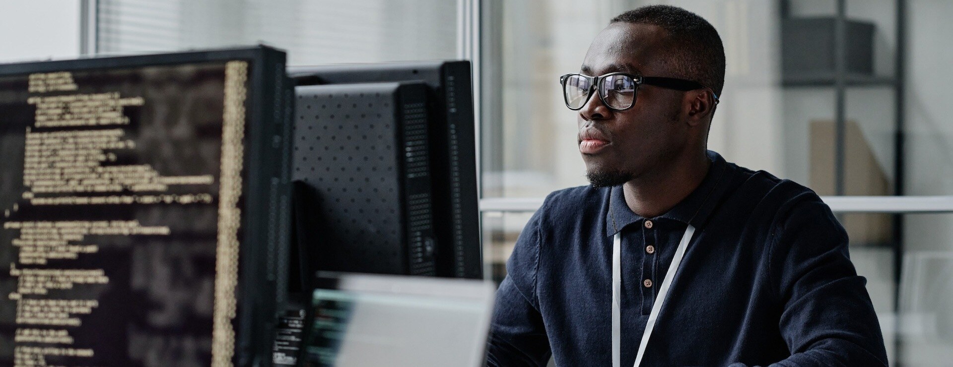 African American young developer in eyeglasses concentrating on his online work on computer sitting at workplace-1